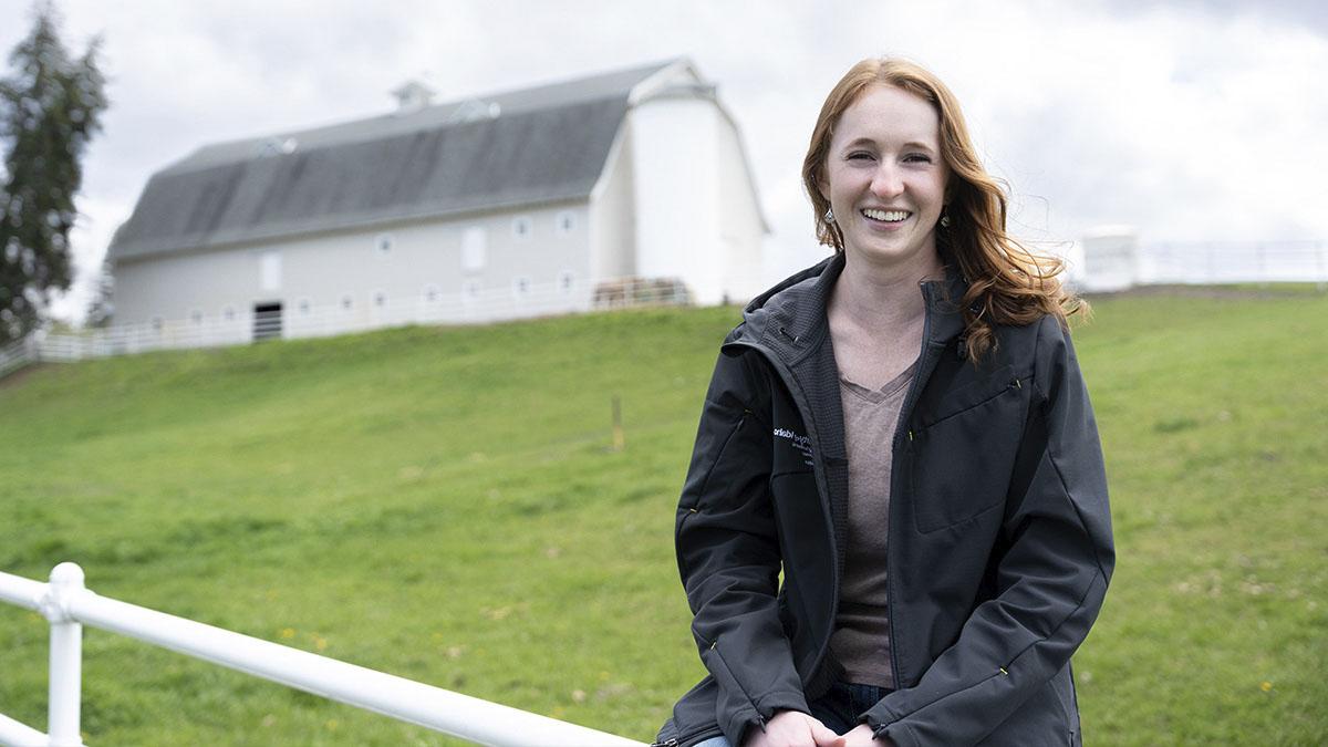 A person sitting on a white fence with a white barn in the background.