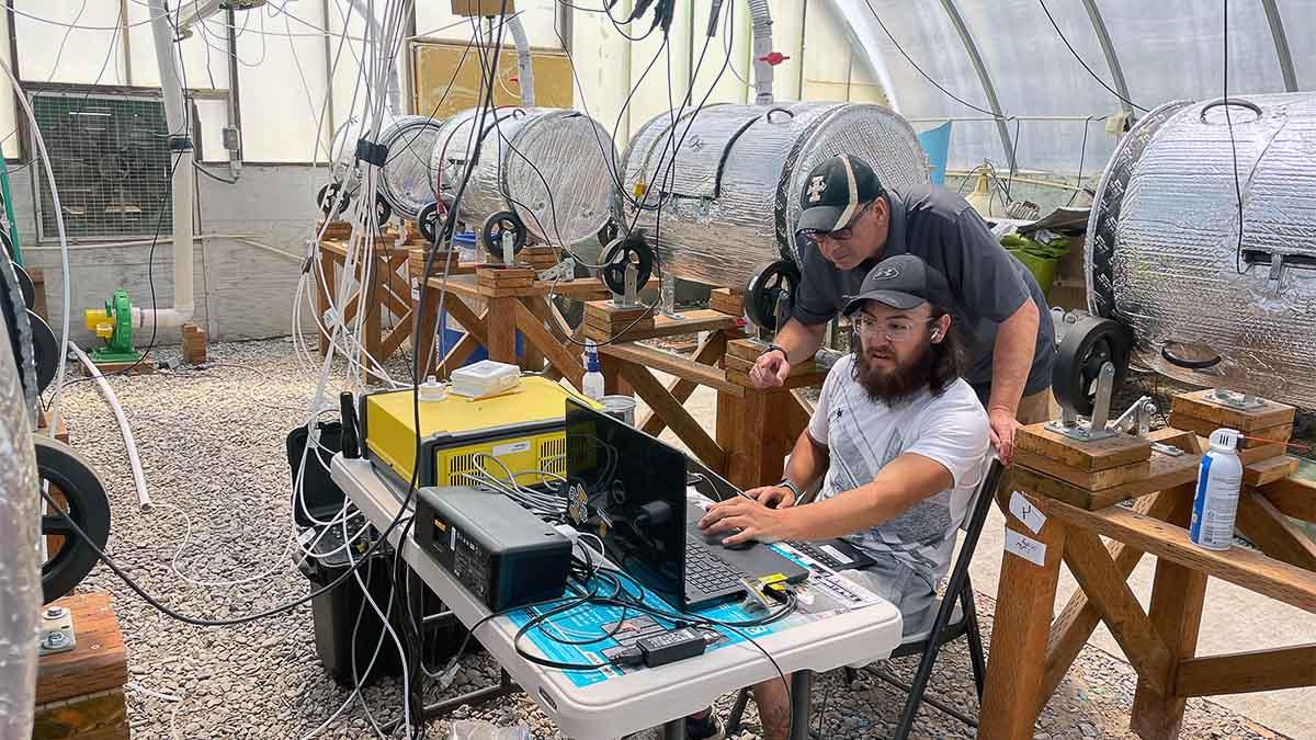 Two men look at a computer in a room with dairy manure composters.