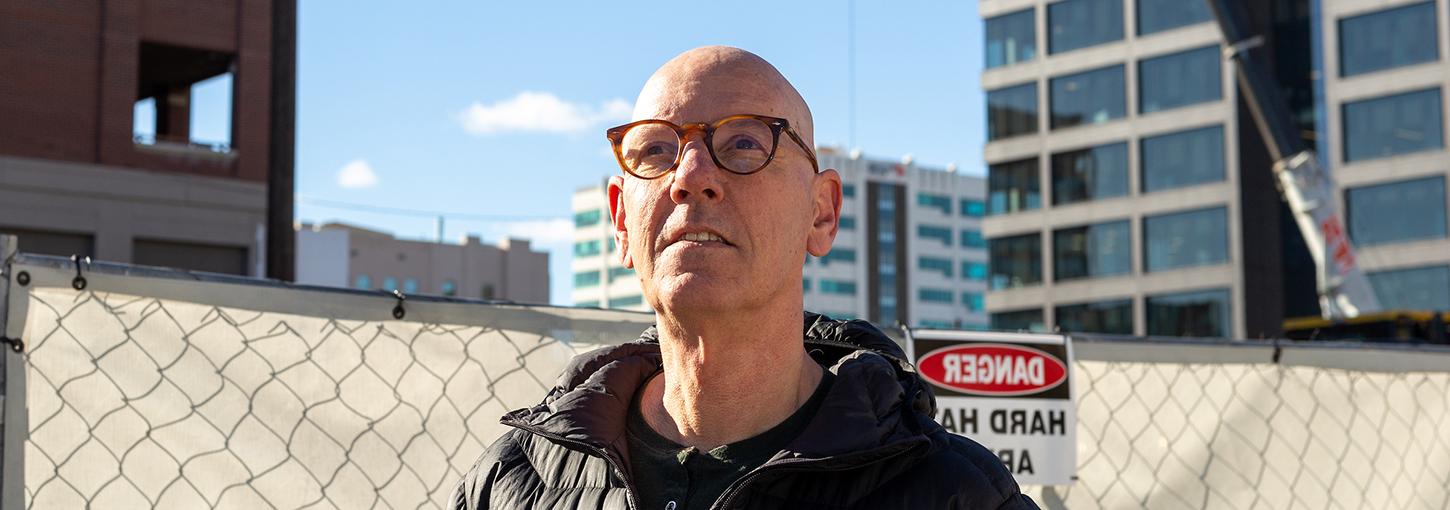 Jaap Vos poses in front of a construction zone fence with a crane and tall buildings in downtown Boise.